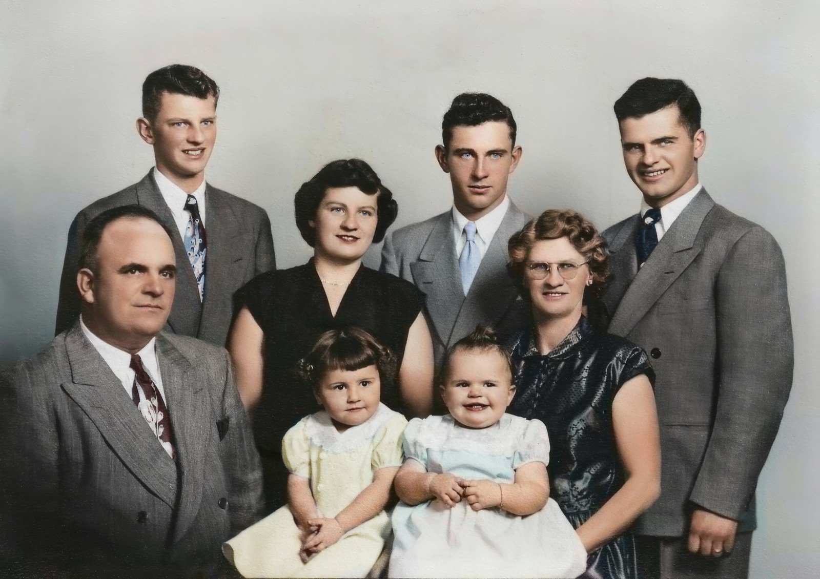A studio portrait of a family: three young men and a young woman standing, the parents, and two small girls in front