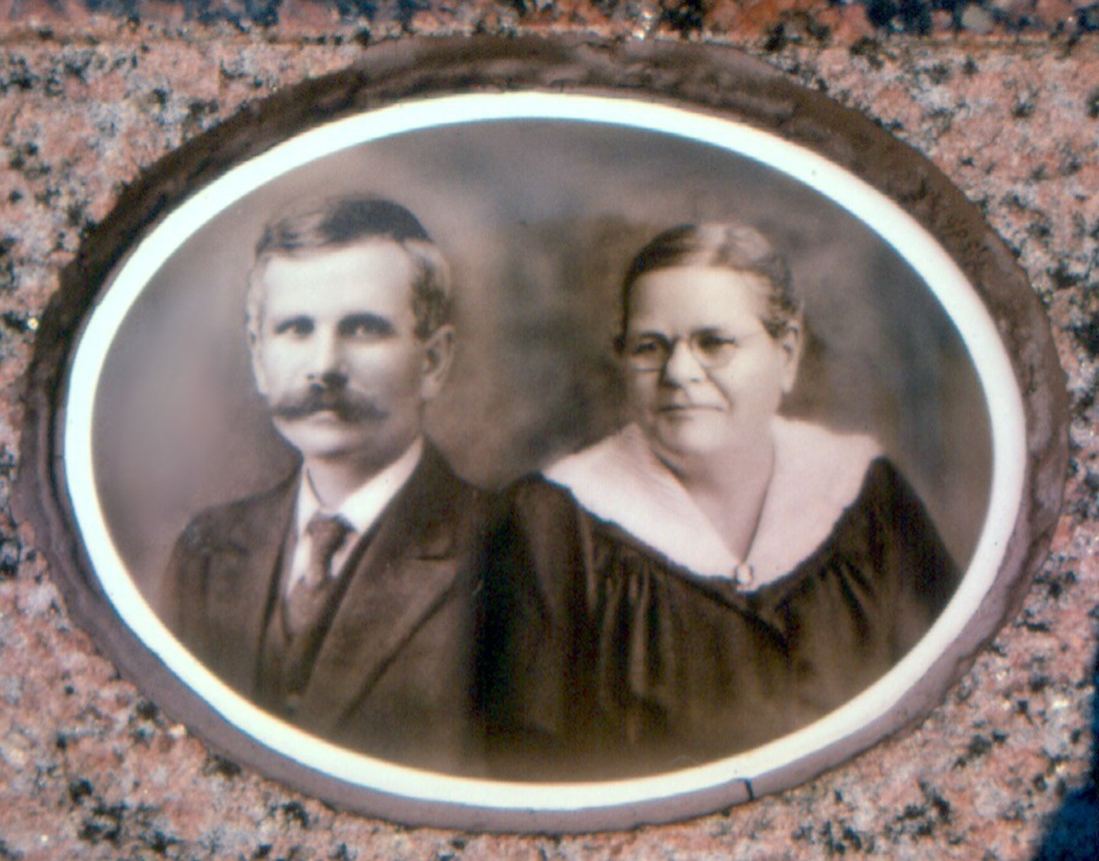 An oval porcelain portrait of a man with a moustache and a woman in glasses, set in granite