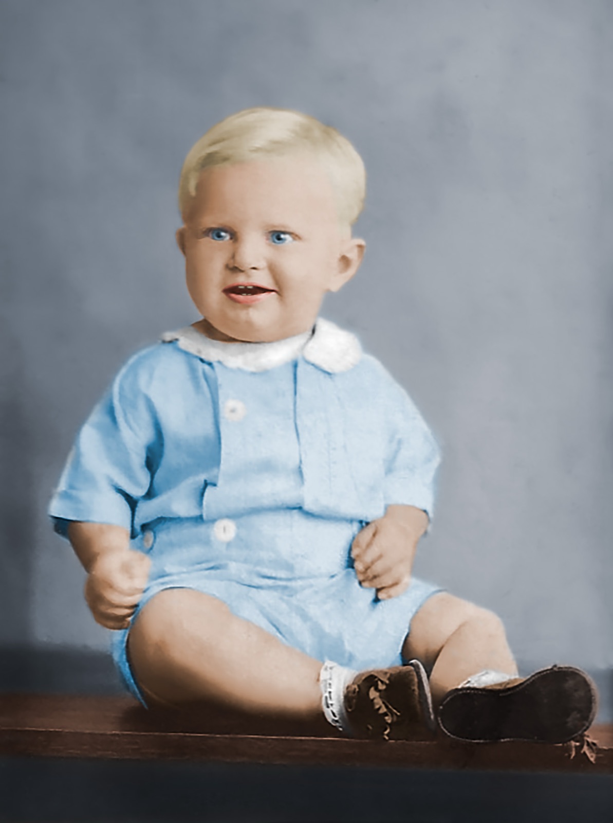 A baby in a pale blue suit, sitting up for a studio portrait