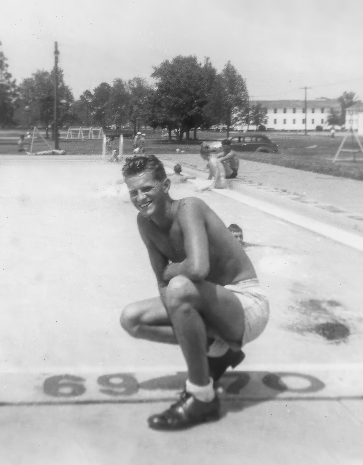 A young sailor in swimming trunks crouching on a pool deck