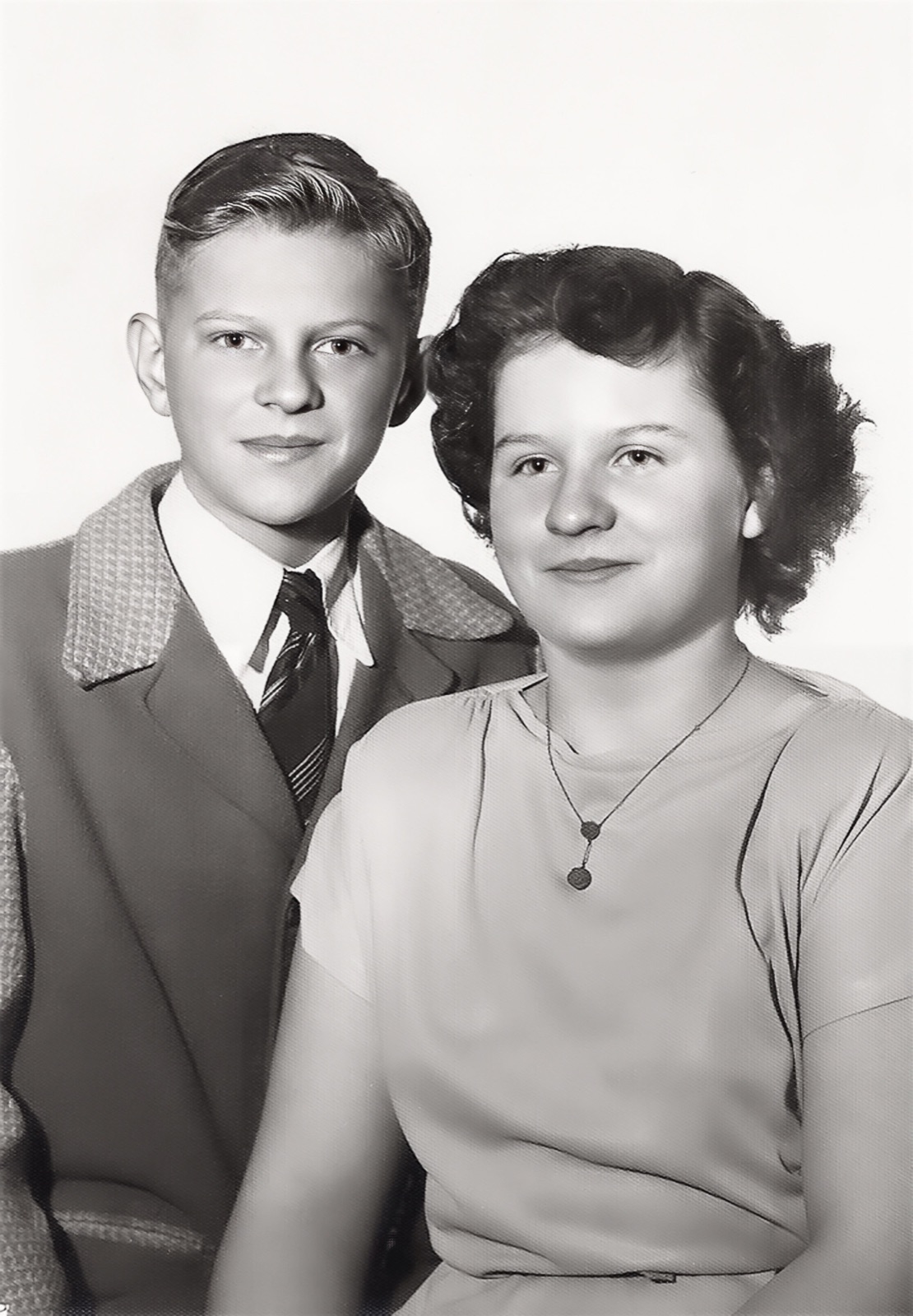 A teenage boy in a jacket and tie beside a teenage girl with dark curled hair