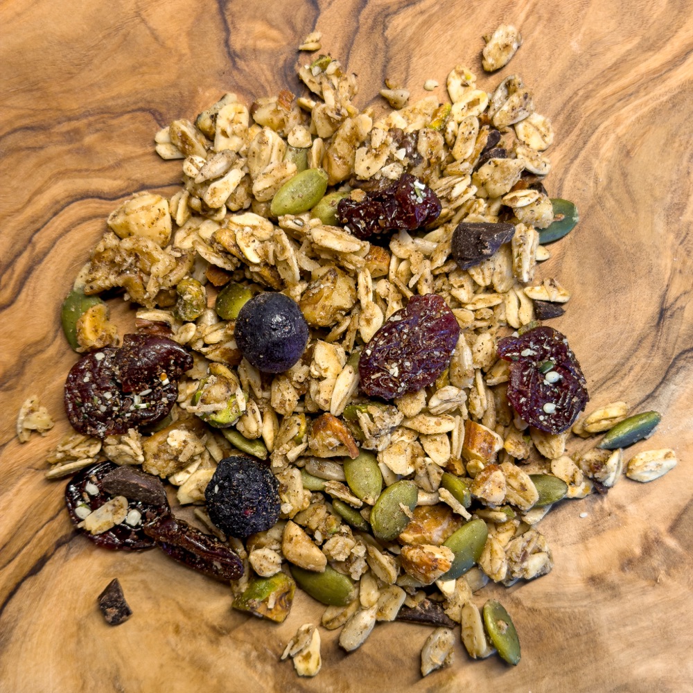A heap of homemade mountain granola with dried cherries, blueberries, pumpkin seeds, and chocolate chunks on an olive wood board